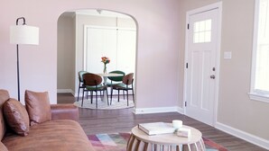 A living room with a brown leather couch, a round wooden coffee table, and a dining area with green chairs and a white table.