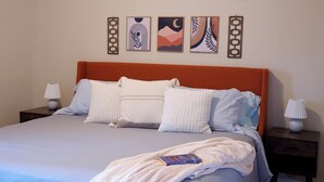 A neatly made bed with a white comforter and multiple pillows, a wooden headboard, and a nightstand with a lamp on each side.