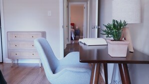 A room with a wooden desk, a chair, a potted plant, and a dresser.