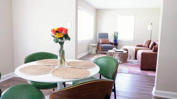 A dining area with a round table, green chairs, and a vase with flowers.
