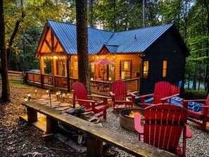 Uma cabana com varanda, cadeiras Adirondack vermelhas, um braseiro e um caminho de pedra.