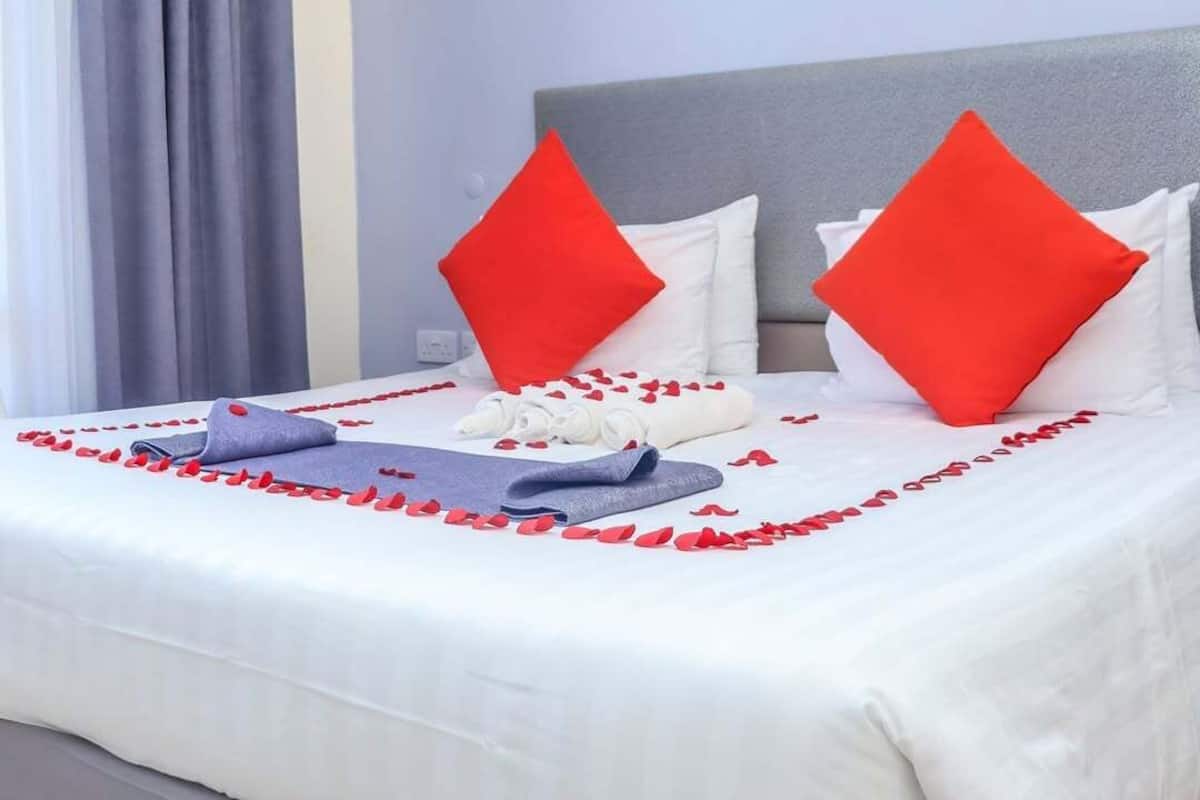 A neatly made bed with white and red pillows, a grey headboard, and a white bedspread.
