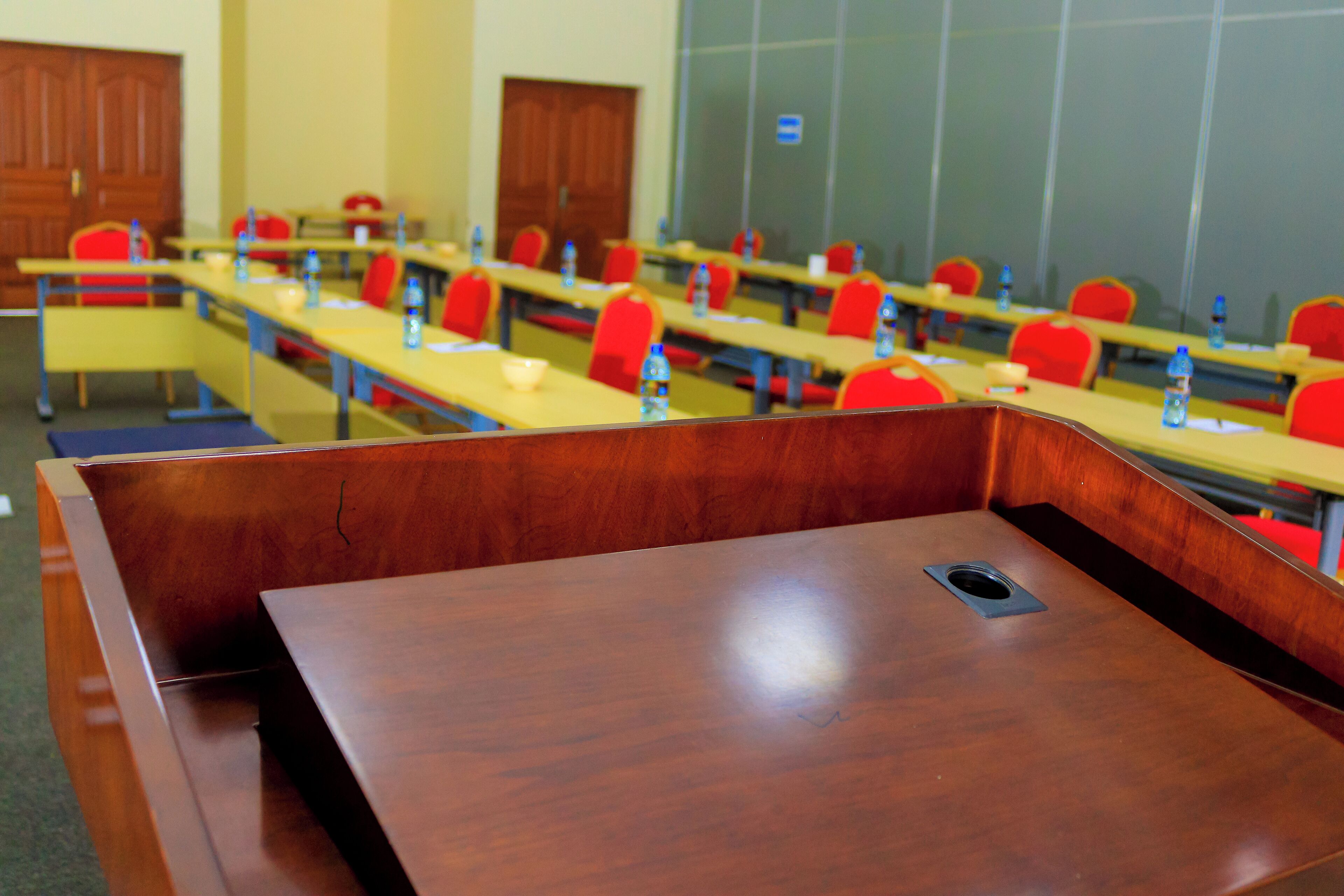 Un salón de conferencias con varias mesas y sillas, equipado con botellas de agua y documentos.