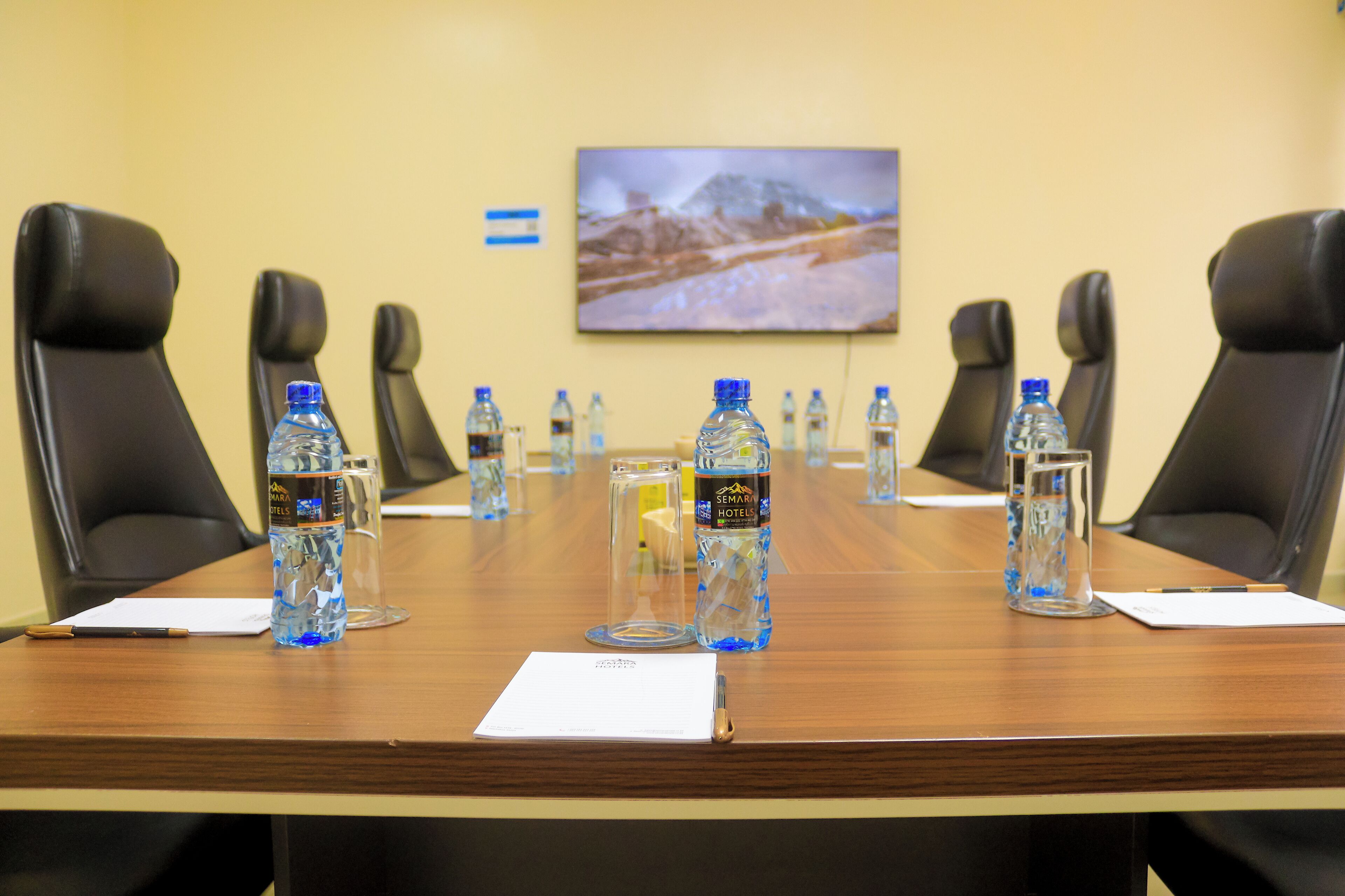 Ein Konferenzraum mit einem langen Tisch, schwarzen Stühlen, Wasserflaschen, Gläsern und einem gerahmten Bild an der Wand.