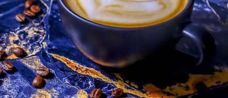 A cup of coffee with latte art on a textured surface with scattered coffee beans.
