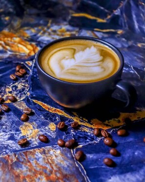 A cup of coffee with latte art on a textured surface with scattered coffee beans. - Semara Hotels Machakos (Machakos)