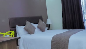 A hotel room with a bed, a nightstand, a lamp, and a window with curtains. - Semara Hotels Machakos (Machakos)