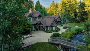 A large house with a covered patio, a small bridge, and a stream.