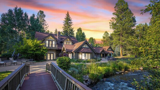 A lodge with multiple buildings, a wooden deck, and a river.