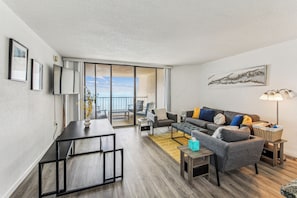 A modern living room with a dining table, sofa, and a view of the outdoors. - Includes Xplorie Activities and Linens. PYRAMID - 1BR oceanfront condo w/outdoor pool. (Ocean City)
