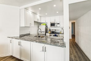 A modern kitchen with white cabinets, a granite countertop, stainless steel appliances, and a wooden floor. - Includes Xplorie Activities and Linens. PYRAMID - 1BR oceanfront condo w/outdoor pool. (Ocean City)