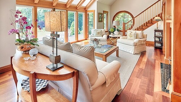 Un salón espacioso con techo alto, ventanas grandes y una escalera que sube a un nivel superior.