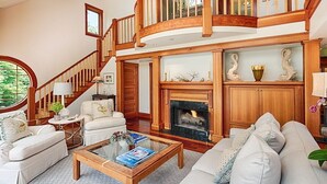 Amplia sala de estar con chimenea, una escalera y vistas al exterior.