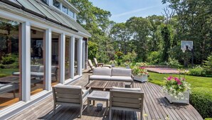 Una terraza con mobiliario exterior, un aro de baloncesto y un jardín con flores.