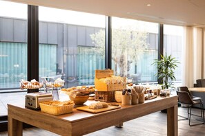 A breakfast buffet with various food items and utensils on a wooden table in a modern room with large windows. - Cultural Weekend Away Close to The Beguinage! Family-friendly Unit w/ Kitchen! (Antwerpen)