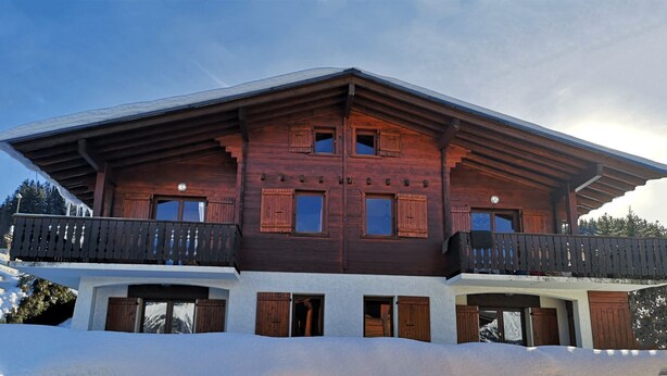 A two-story wooden chalet with a balcony on the upper floor, surrounded by snow. - Chalet "Les Mouflons" - Le Clos - Sleeps 8, 5 minutes walk from the ski slopes (Crest-Voland)