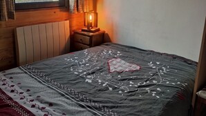 A bedroom with a bed, a nightstand with a lamp, a window with curtains, and a view of mountains. - Chalet "Les Mouflons" - Le Clos - Sleeps 8, 5 minutes walk from the ski slopes (Crest-Voland)