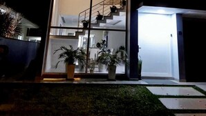 A modern house with a large glass facade, a staircase leading to an upper level, and potted plants in the foreground.