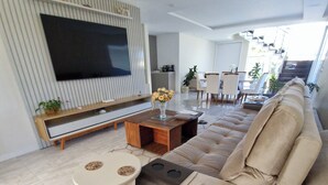 A modern living room with a large flat-screen TV, a beige sectional sofa, a coffee table, and a small side table.