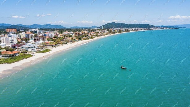 An aerial view of a coastal city with a long sandy beach, clear turquoise waters, and a boat in the distance.