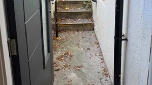 Una escalera estrecha que conduce a un edificio blanco con una puerta negra y barandales de metal.