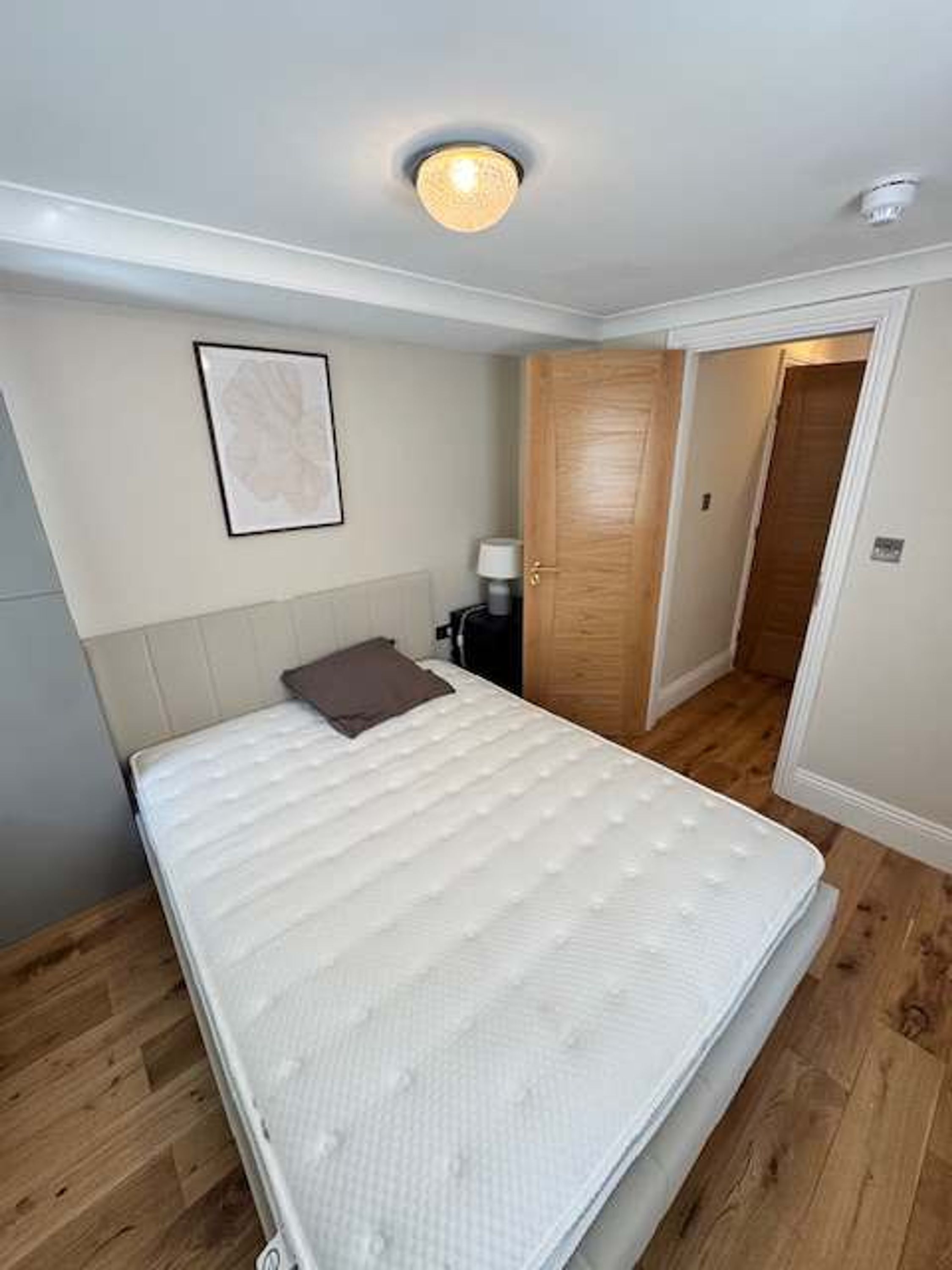 A bedroom with a bed, a nightstand, a lamp, and a door leading to another room.