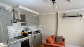 Una cocina moderna con armarios grises, un microondas y una estufa a gas. Hay piso de madera y un sofá rojo en la sala de estar.