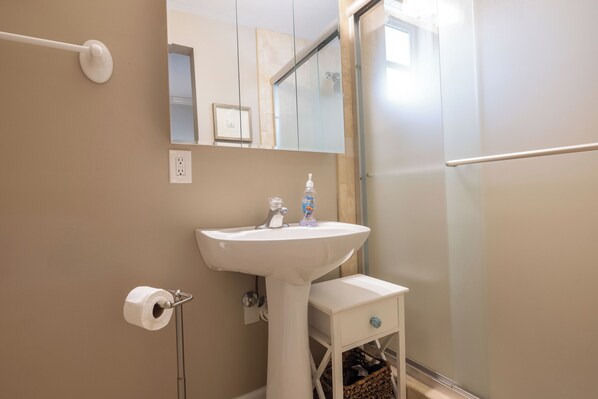 Une salle de bain avec un lavabo blanc, un miroir, un porte-serviettes et un espace douche.
