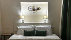 Een hotelkamer met een bed, twee bedlampen, een decoratief wandobject en een groen gordijn.