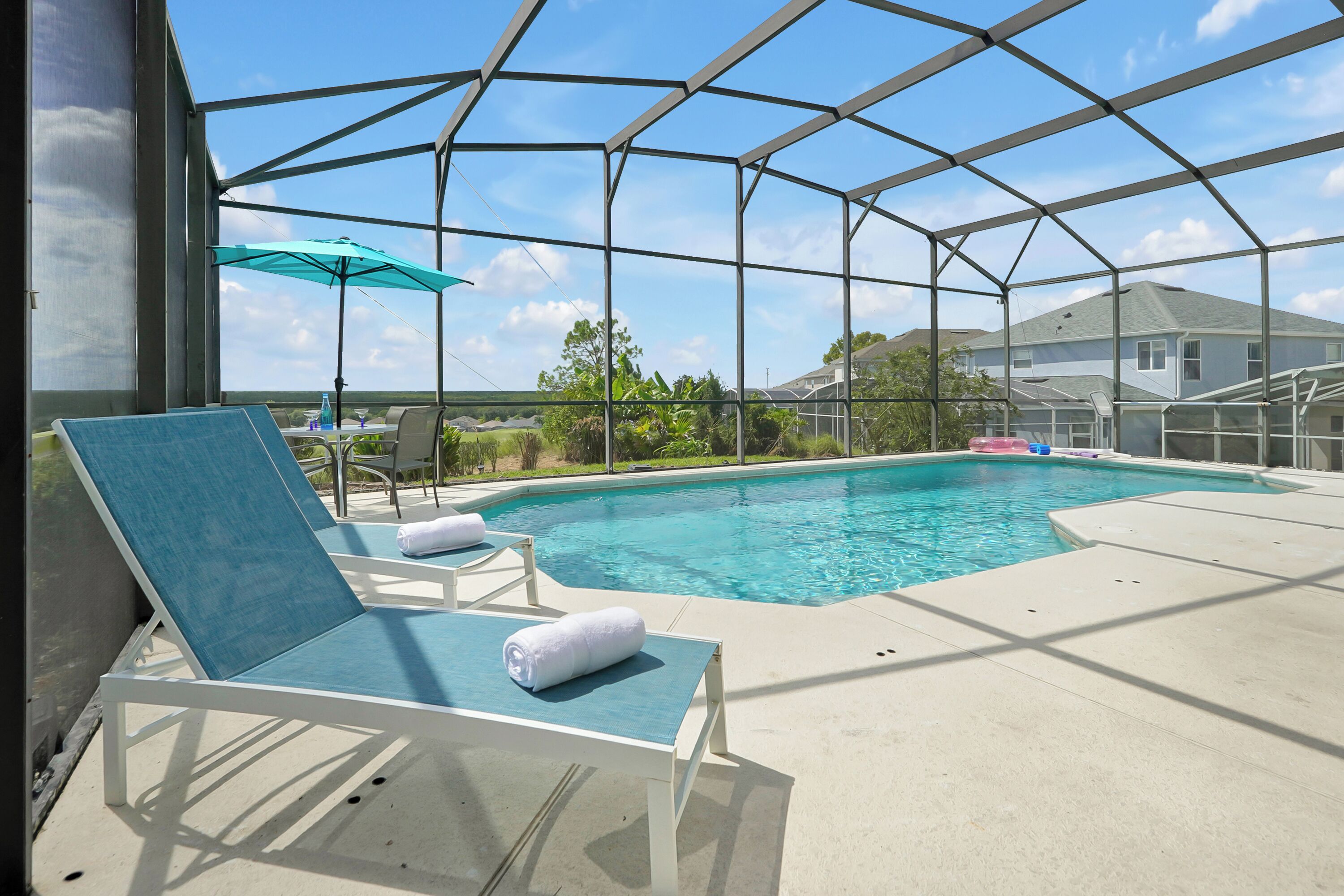 Une piscine extérieure couverte, dotée de chaises longues et d’une table, et entourée d’une structure en métal.