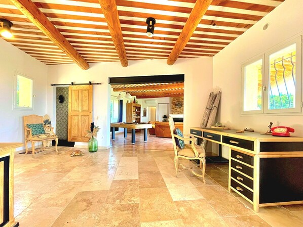 A spacious room with a wooden ceiling, a billiards table, and a desk with drawers.