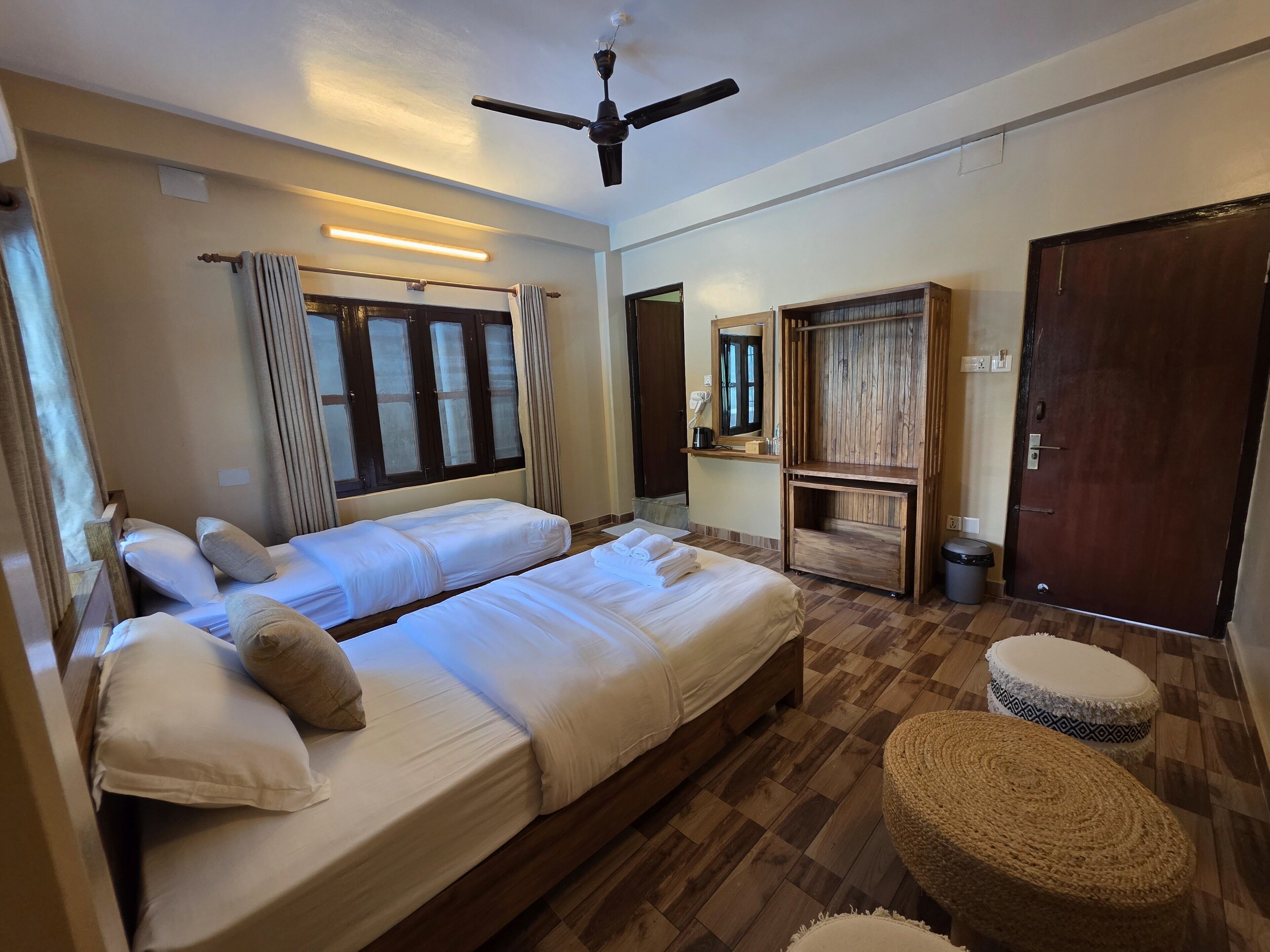 A hotel room with two beds, a ceiling fan, a wooden bench, and a small table with a mirror.