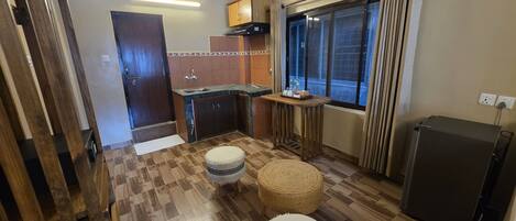 Una cocina compacta con horno empotrado, un pequeño comedor con taburetes y una ventana con cortinas.