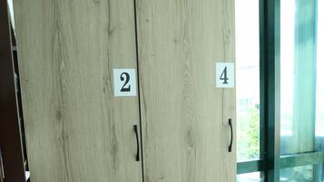 A wooden wardrobe with four numbered compartments, located in a room with a glass door and a view of greenery outside.