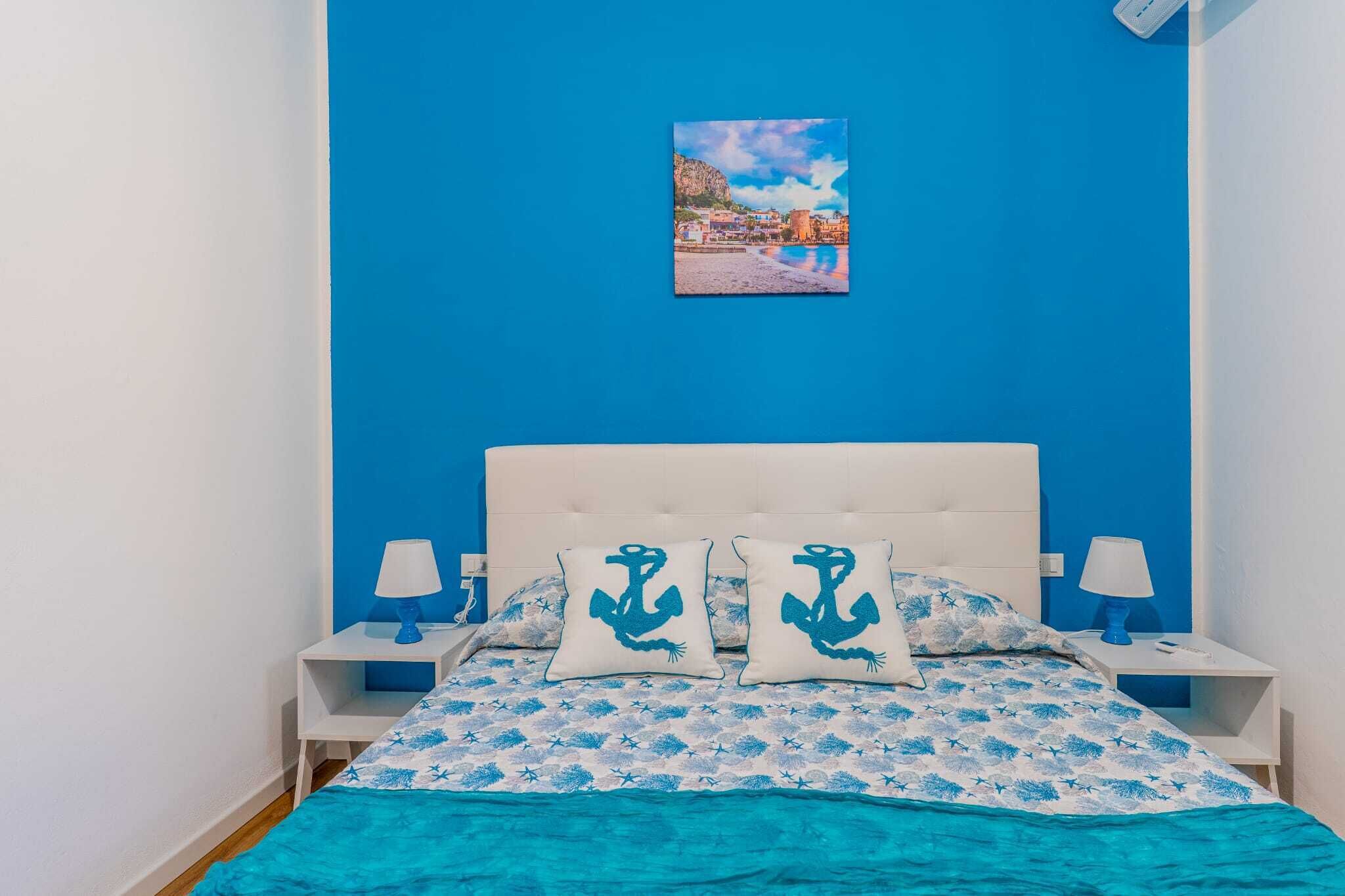 Ein Schlafzimmer mit blauer Wand, einem Bett mit weißem Kopfteil, zwei Nachttischen und passenden Lampen.