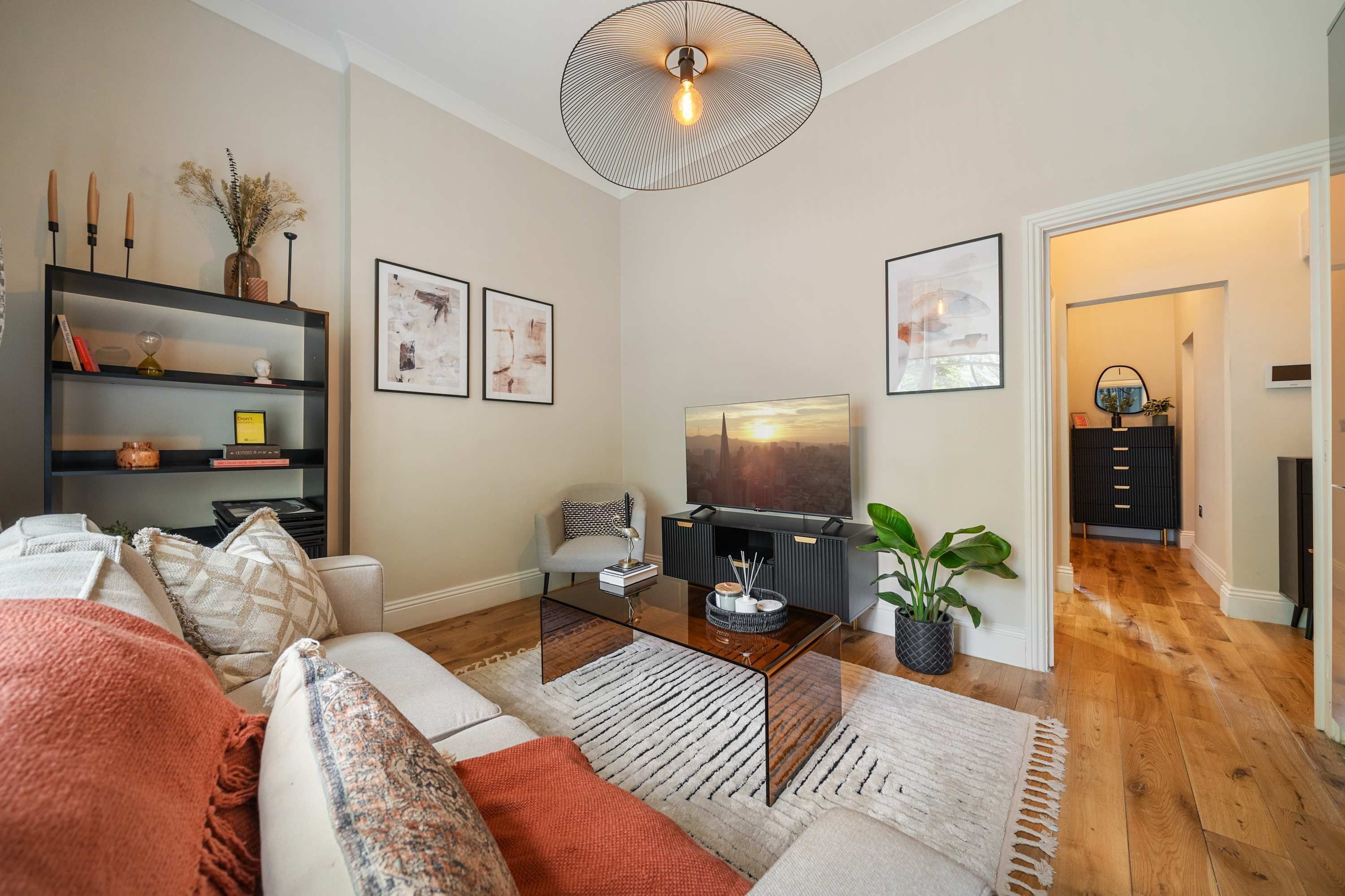 A modern living room with a sofa, coffee table, and TV. There is a bookshelf, a plant, and artwork on the walls.