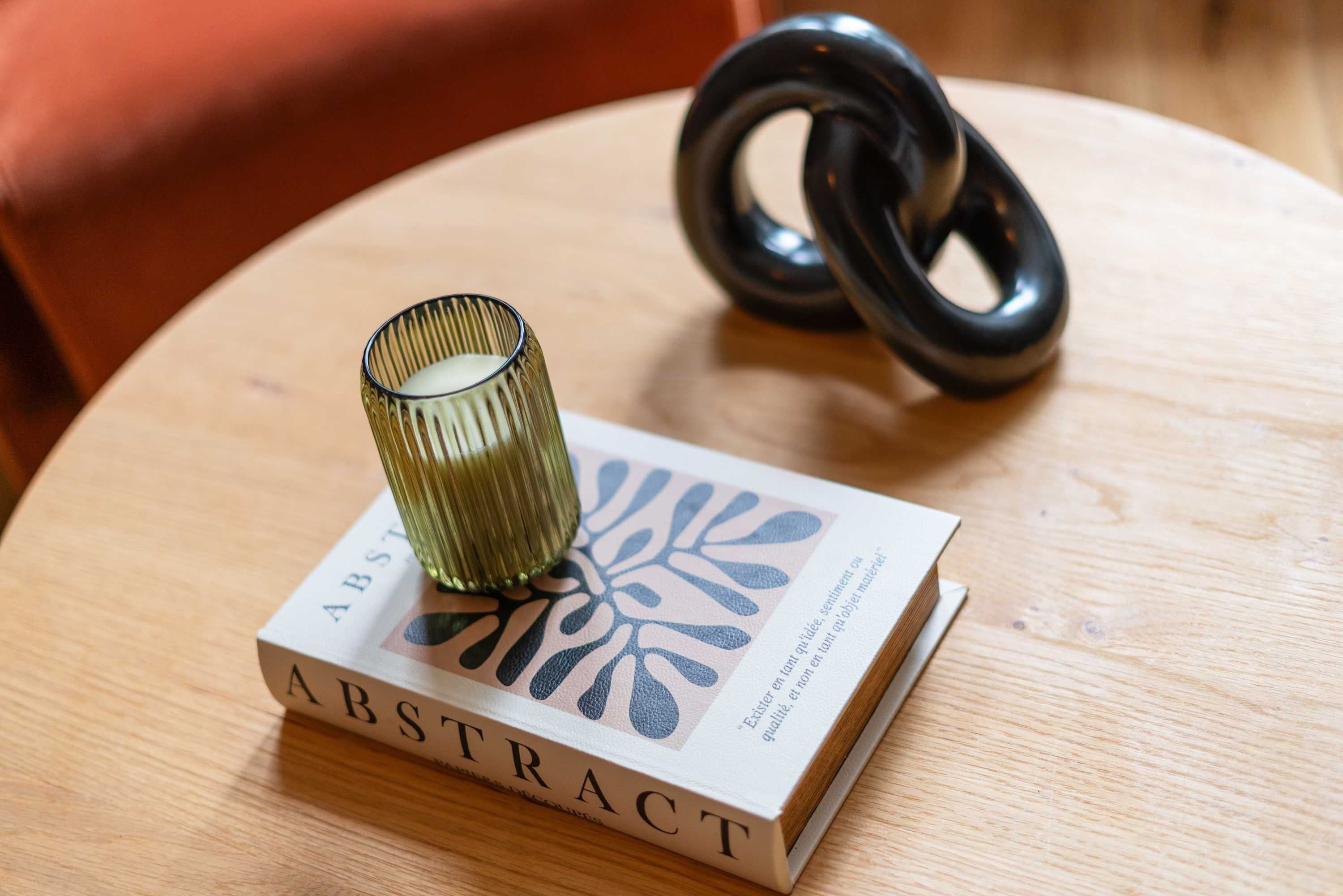 A book titled "ABSTRACT" on a wooden table with a decorative glass object and a black ring.