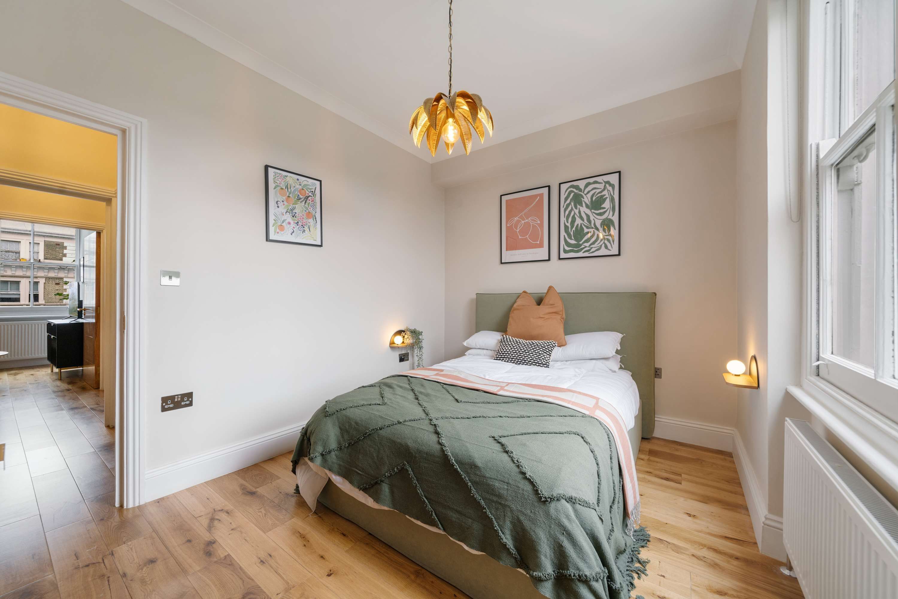 A bedroom with a bed, a green bedspread, a hanging light fixture, and two wall-mounted lights.