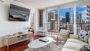Ein modernes Wohnzimmer mit großem Fenster, einer Couch, einem Couchtisch und einem an der Wand befestigten Fernseher.