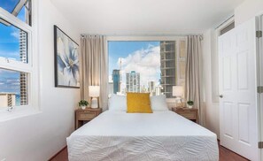 A hotel room with a large bed, two bedside tables, a window with curtains, and a city view.