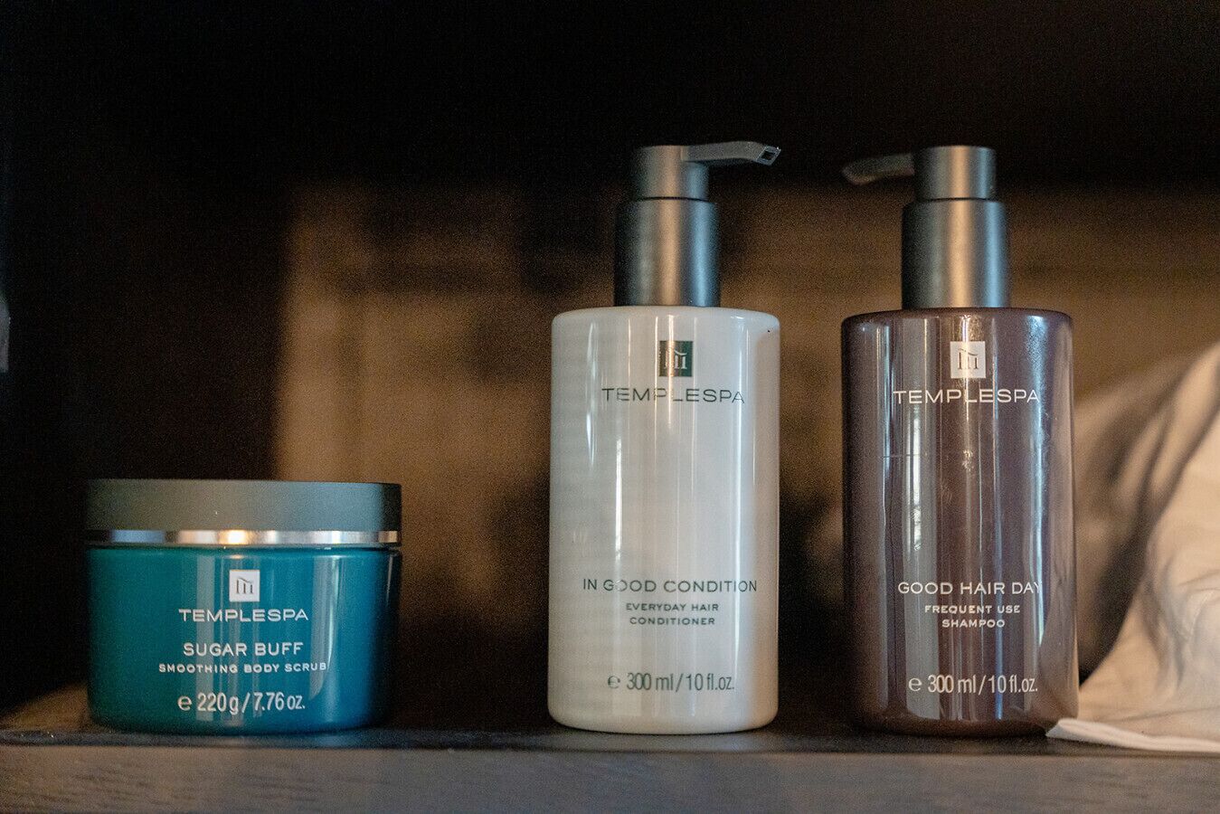 Tres productos TempleSpa: un tarro azul etiquetado 'Sugar Buff', un frasco blanco etiquetado 'Acondicionador para el cabello In Good Condition Everyday' y un frasco marrón etiquetado 'Champú Good Hair Day'.
