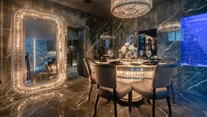 Un comedor lujoso con una mesa redonda, sillas elegantes y un espejo grande con marco iluminado.