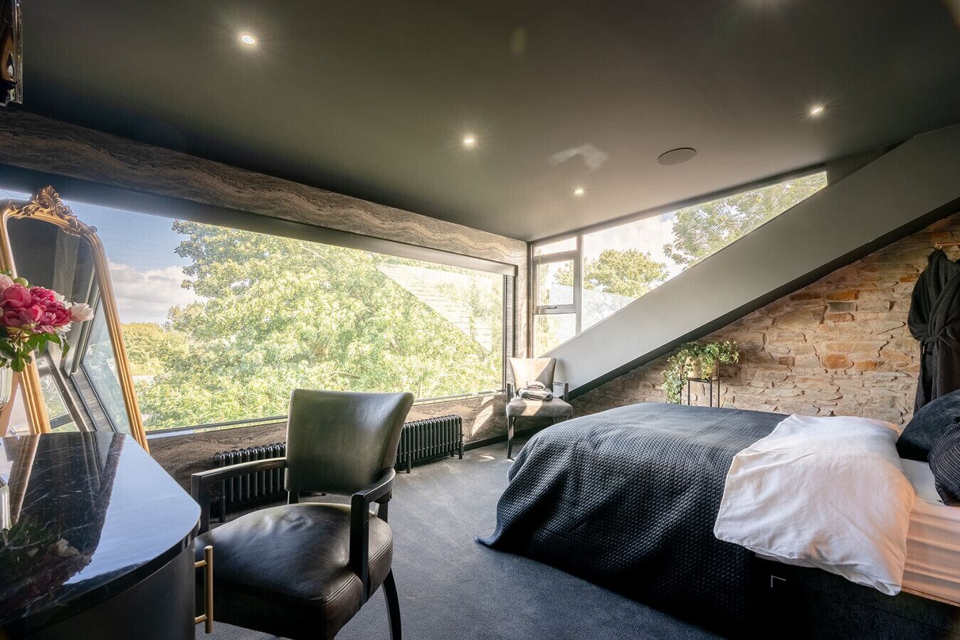 A bedroom with a large window, a bed, a chair, and a radiator.
