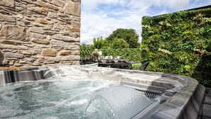 Un jacuzzi con una pared de piedra y un seto verde exuberante al fondo.