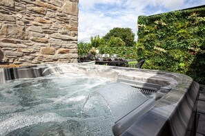 A hot tub with a stone wall and a lush green hedge in the background.