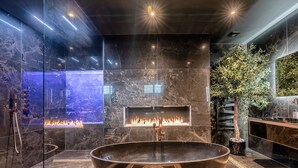 Un baño moderno con una bañera independiente grande, una chimenea empotrada y una zona de ducha con mampara de cristal.