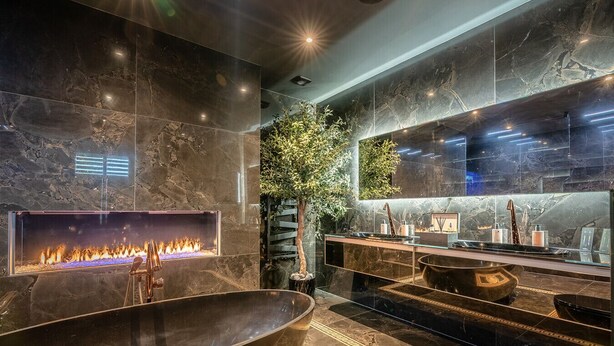 Un baño moderno con una bañera independiente grande, una chimenea integrada y un espejo amplio.