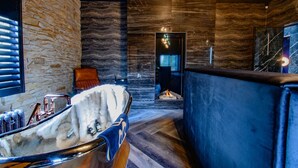 Un baño moderno con pared de piedra, una bañera, un espejo y un banco tapizado en azul.