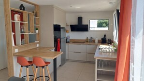 A modern kitchen with a wooden countertop, two red bar stools, a built-in oven, and a window with a view of trees.