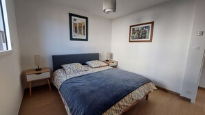 A bedroom with a bed, two bedside tables, a nightstand, a lamp, and two framed pictures on the wall.